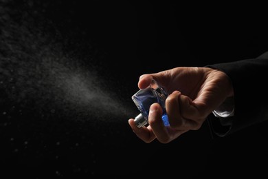 Photo of Man spraying luxury perfume on dark background, closeup. Space for text