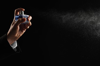 Photo of Man spraying luxury perfume on dark background, closeup. Space for text