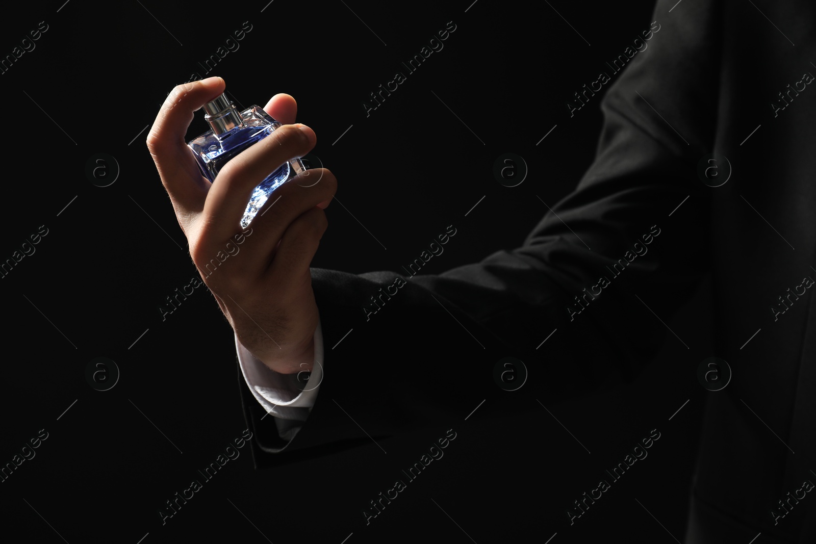 Photo of Man spraying luxury perfume on dark background, closeup