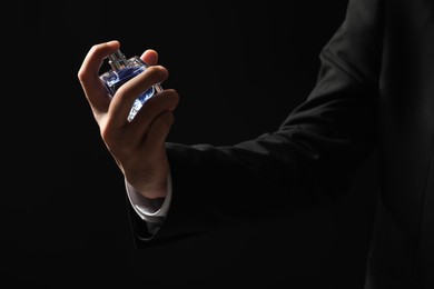 Photo of Man spraying luxury perfume on dark background, closeup