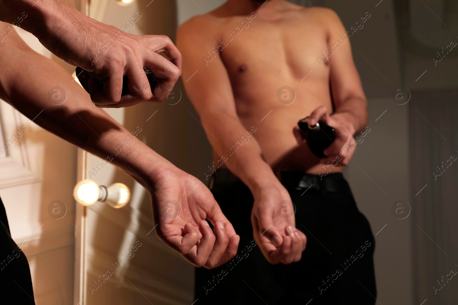 Photo of Man spraying luxury perfume near mirror indoors, closeup