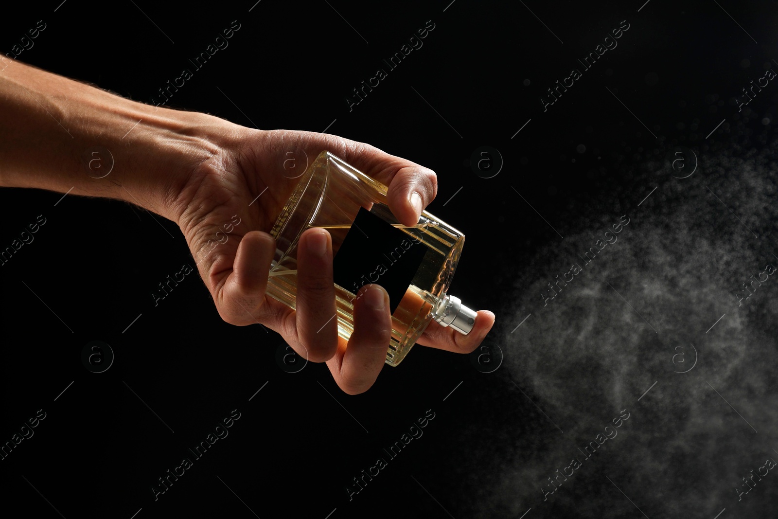 Photo of Man spraying luxury perfume on dark background, closeup