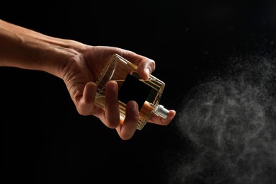 Photo of Man spraying luxury perfume on dark background, closeup