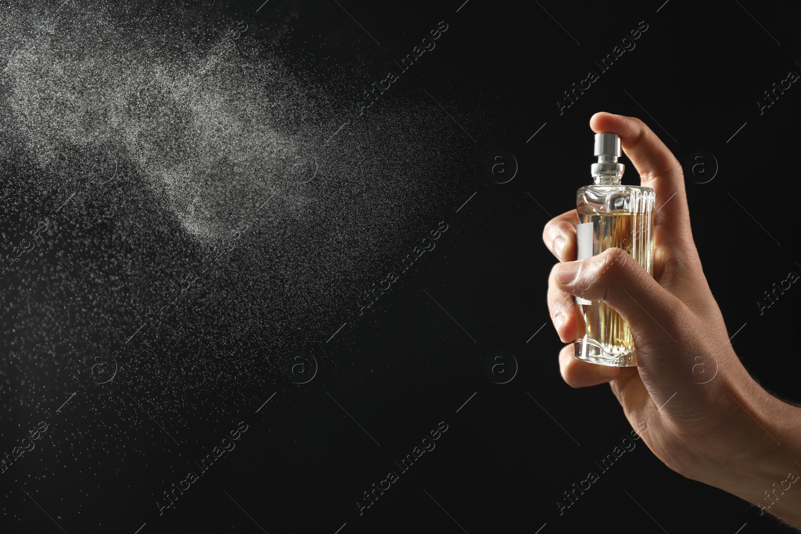 Photo of Man spraying luxury perfume on dark background, closeup. Space for text