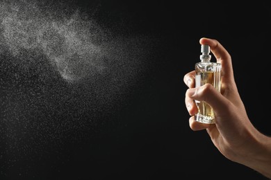 Man spraying luxury perfume on dark background, closeup. Space for text