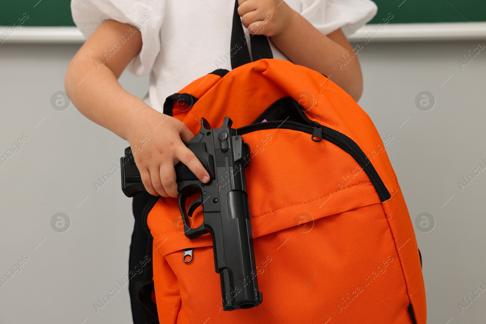Photo of Child with gun and backpack in classroom, closeup. School shooting
