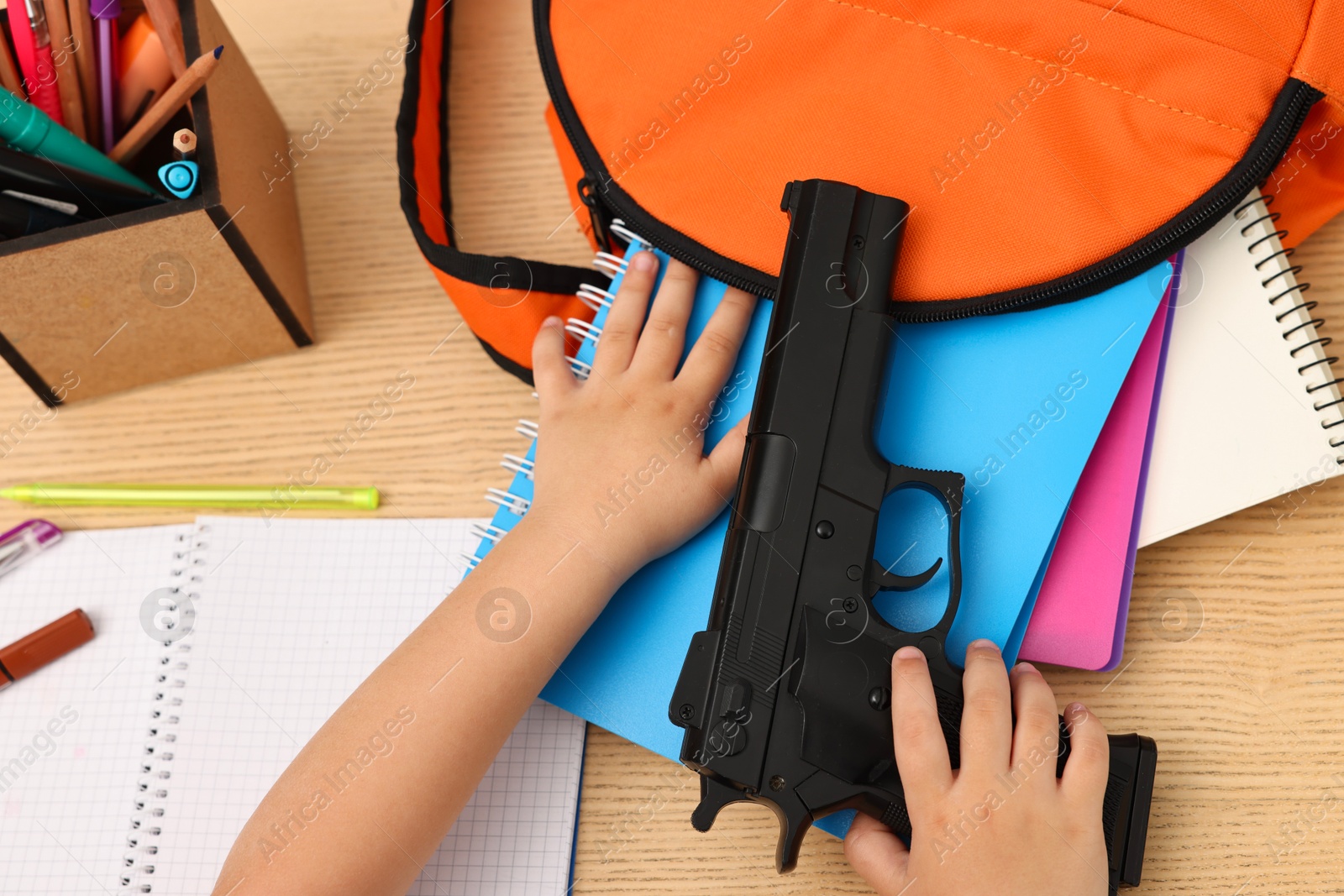 Photo of Child with gun and school stationery at desk, closeup