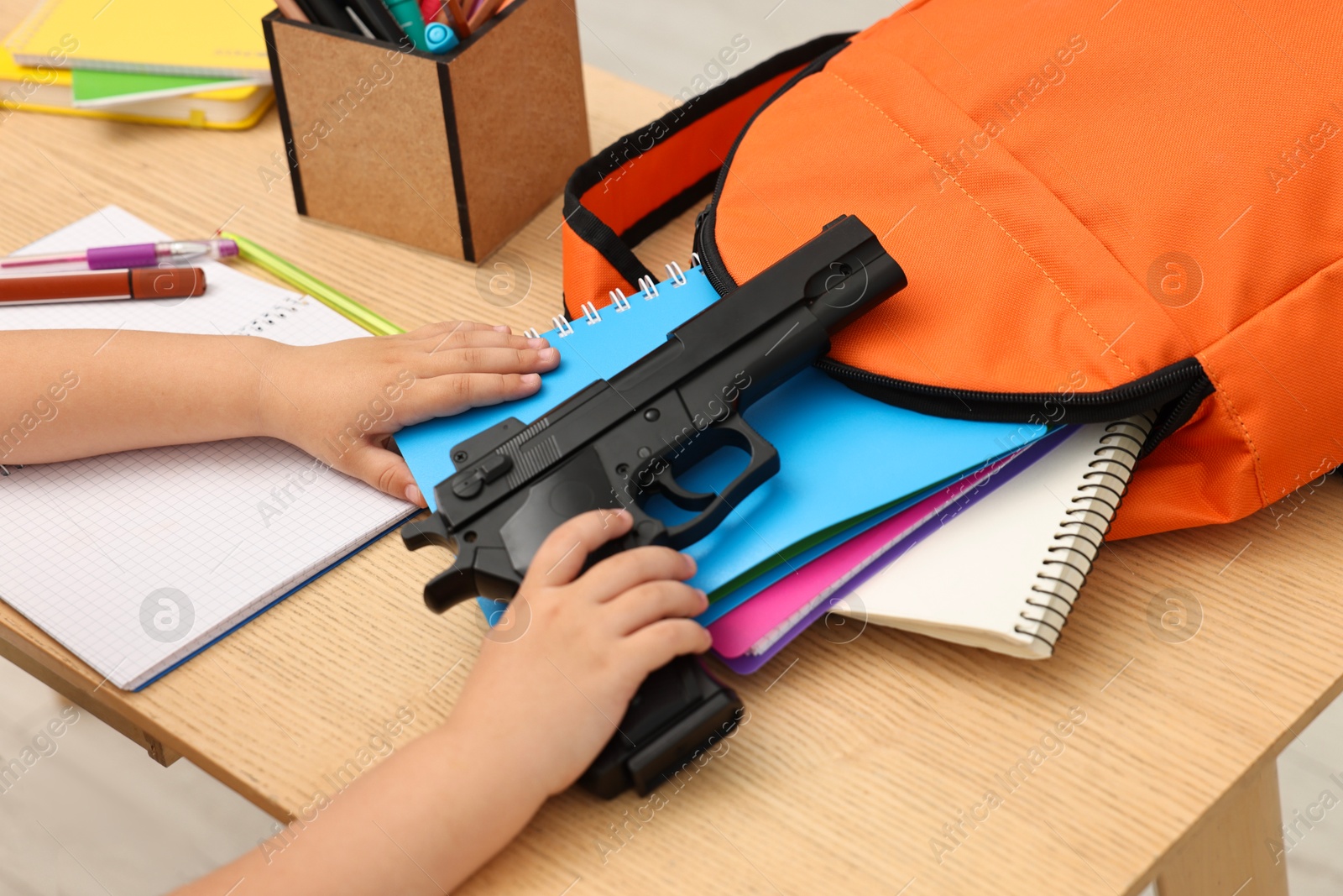 Photo of Child with gun and school stationery at desk, closeup