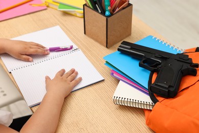 Photo of Child at desk with school stationery and gun, closeup