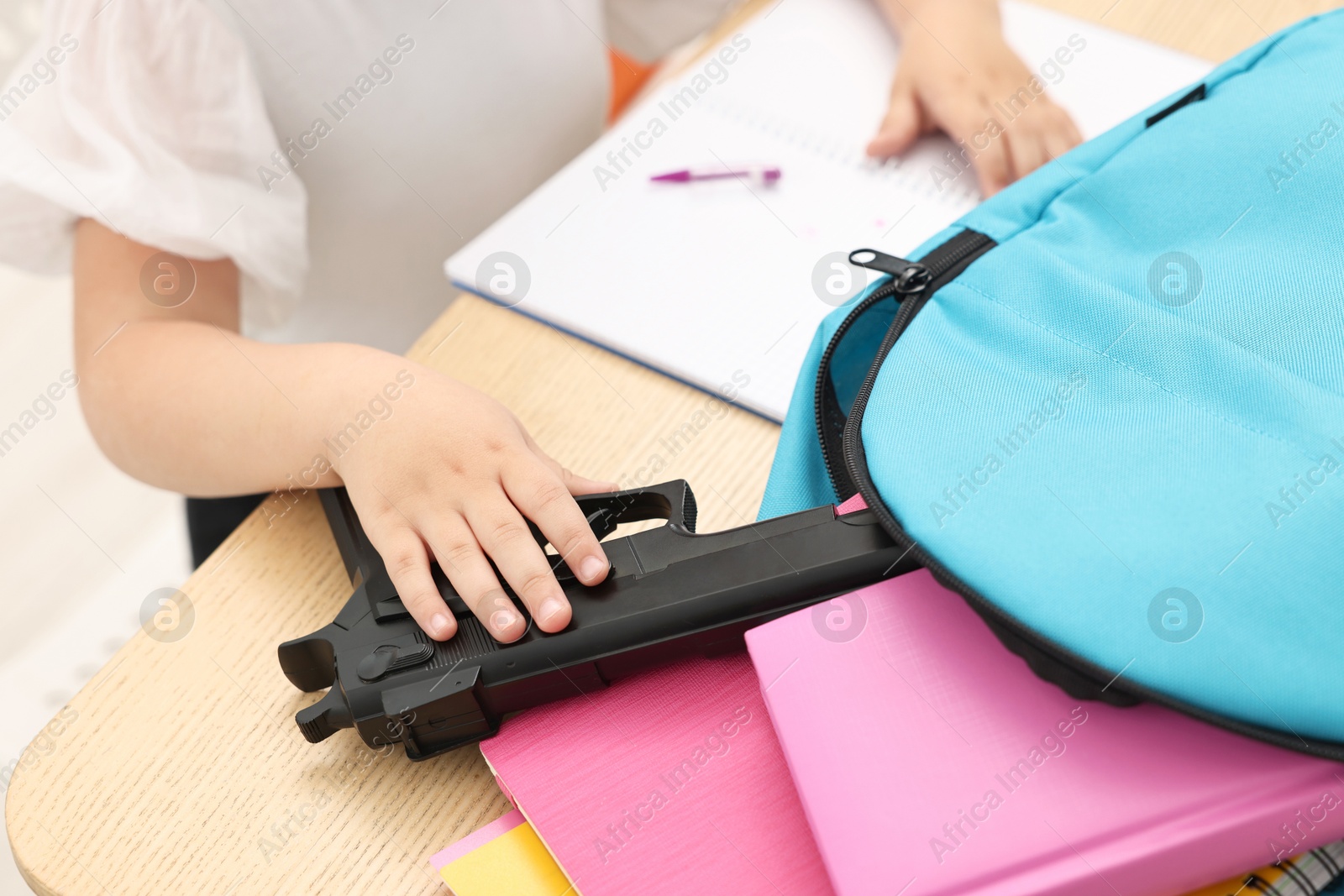 Photo of Child taking gun out of backpack at desk in classroom, closeup. School shooting