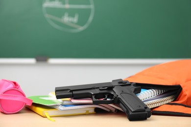 School stationery and gun on desk in classroom, closeup