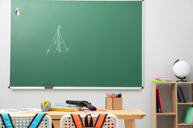 Photo of School stationery and gun on desk in classroom