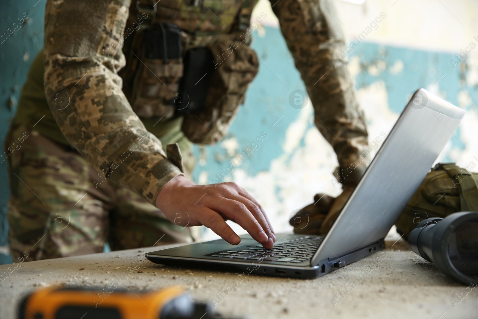 Photo of Military mission. Soldier in uniform using laptop at table inside abandoned building, closeup
