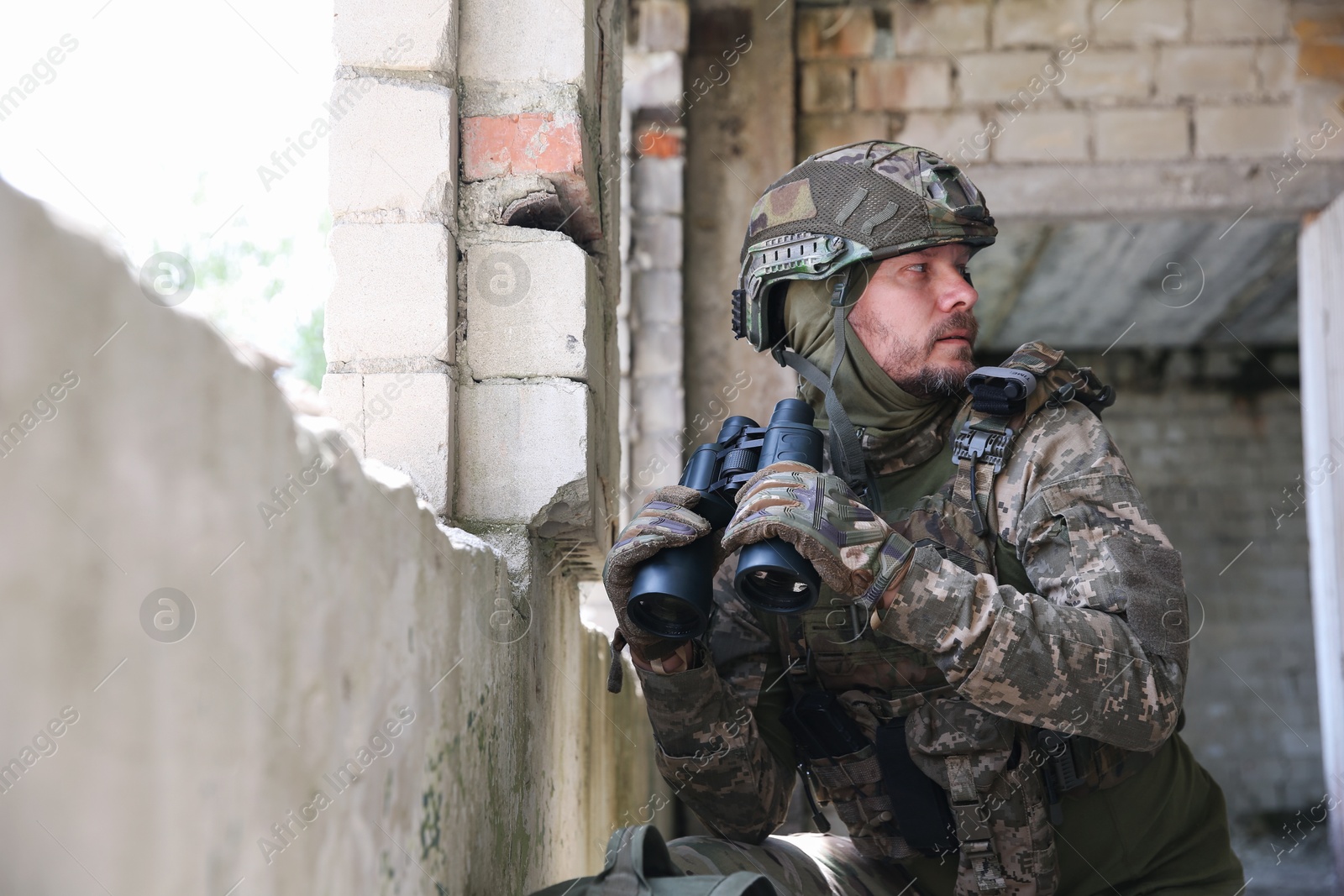 Photo of Military mission. Soldier in uniform with binoculars inside abandoned building, space for text