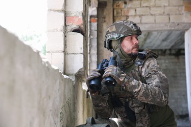 Military mission. Soldier in uniform with binoculars inside abandoned building, space for text