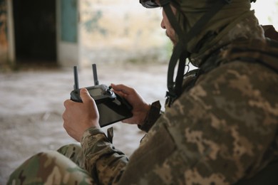 Photo of Military mission. Soldier in uniform with drone controller inside abandoned building, closeup