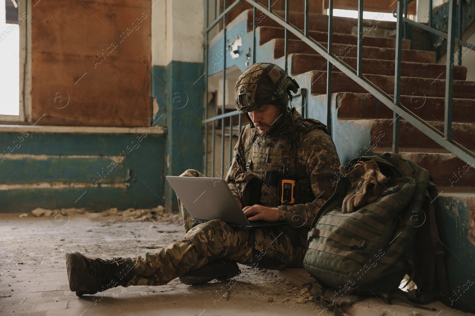 Photo of Military mission. Soldier in uniform using laptop inside abandoned building