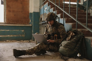 Photo of Military mission. Soldier in uniform using laptop inside abandoned building