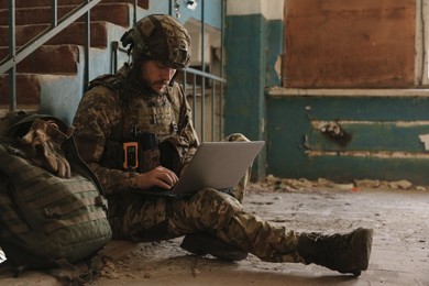 Military mission. Soldier in uniform using laptop inside abandoned building