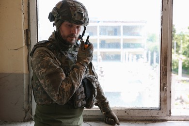 Photo of Military mission. Soldier in uniform with radio transmitter inside abandoned building, space for text