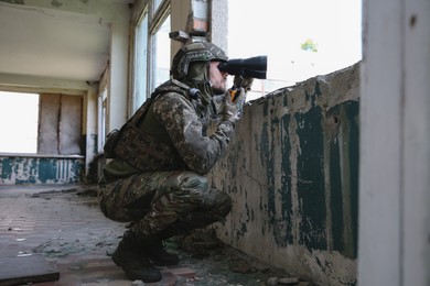 Photo of Military mission. Soldier in uniform with binoculars inside abandoned building