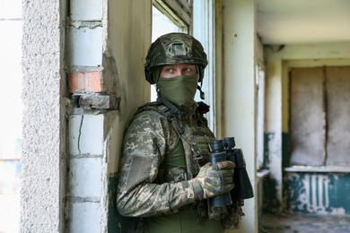 Military mission. Soldier in uniform with binoculars inside abandoned building