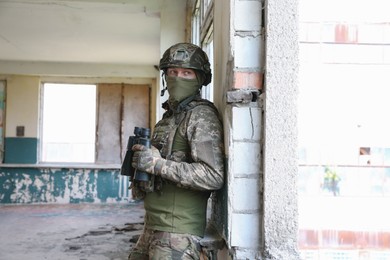 Military mission. Soldier in uniform with binoculars inside abandoned building