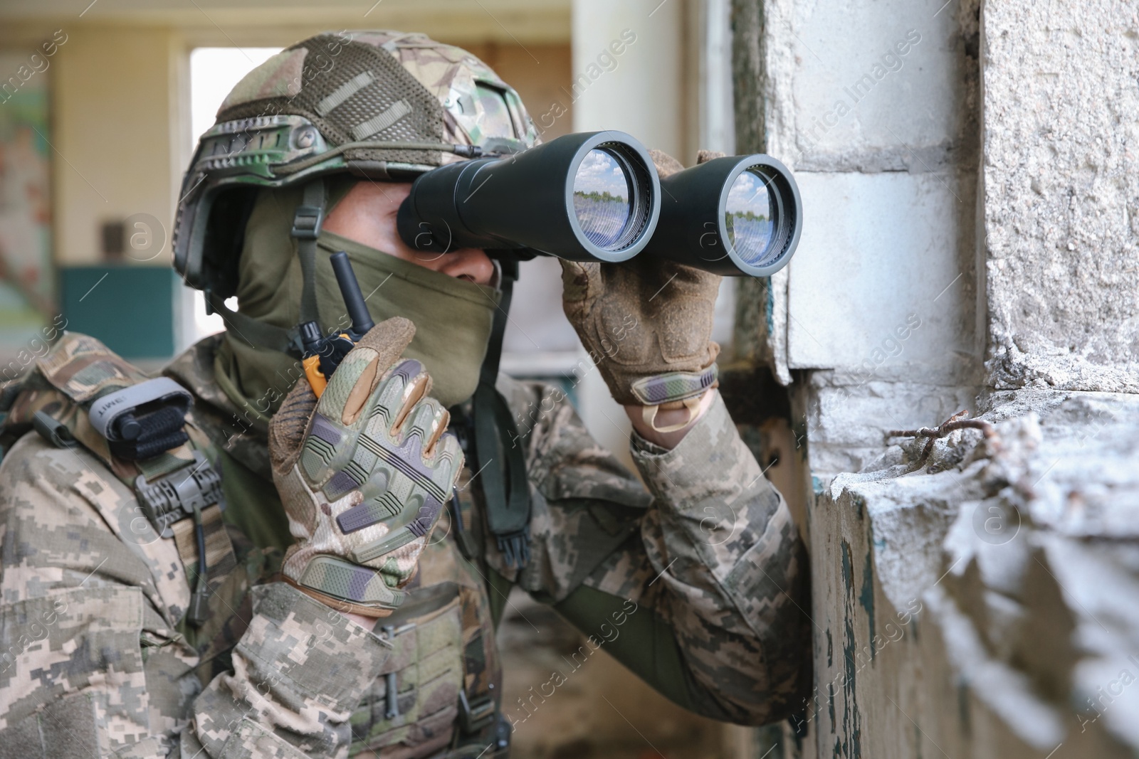 Photo of Military mission. Soldier in uniform with binoculars inside abandoned building