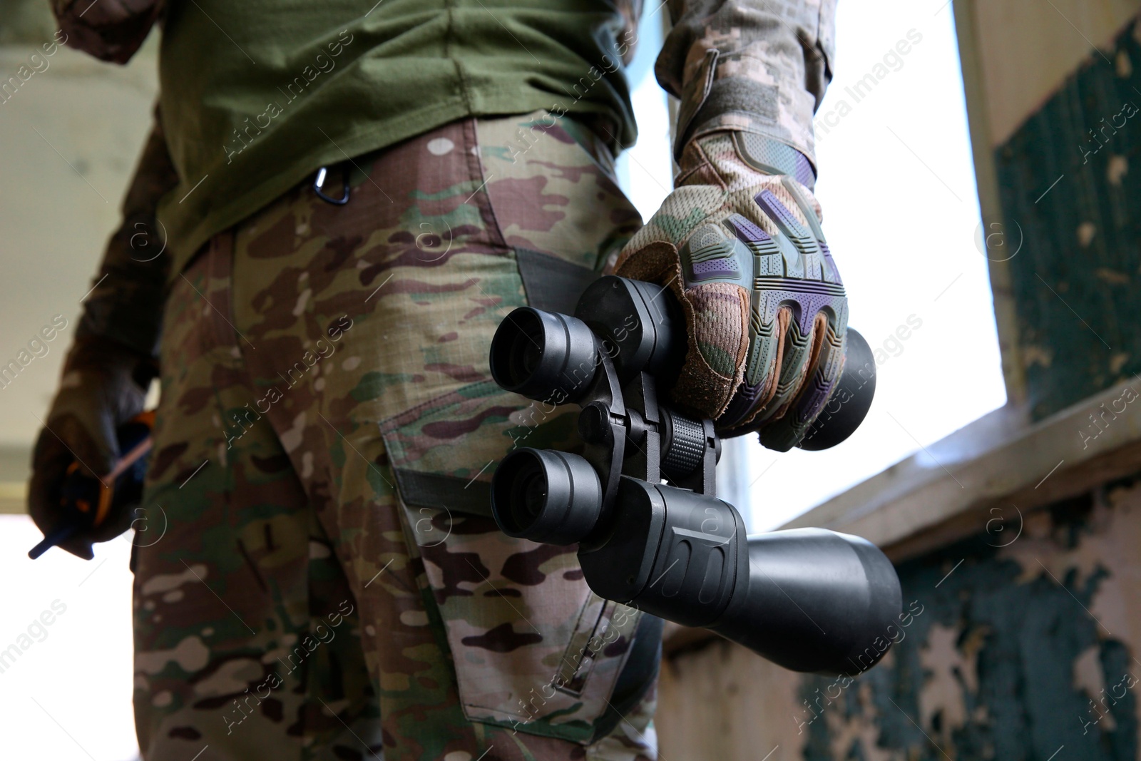 Photo of Military mission. Soldier in uniform with binoculars inside abandoned building, closeup