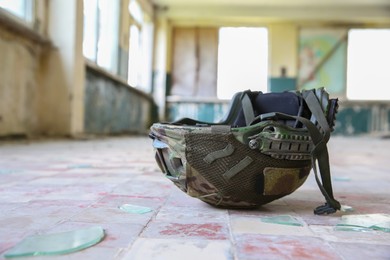 Military mission. Camouflage helmet on floor inside abandoned building, closeup. Space for text