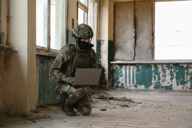 Military mission. Soldier in uniform using laptop inside abandoned building, space for text