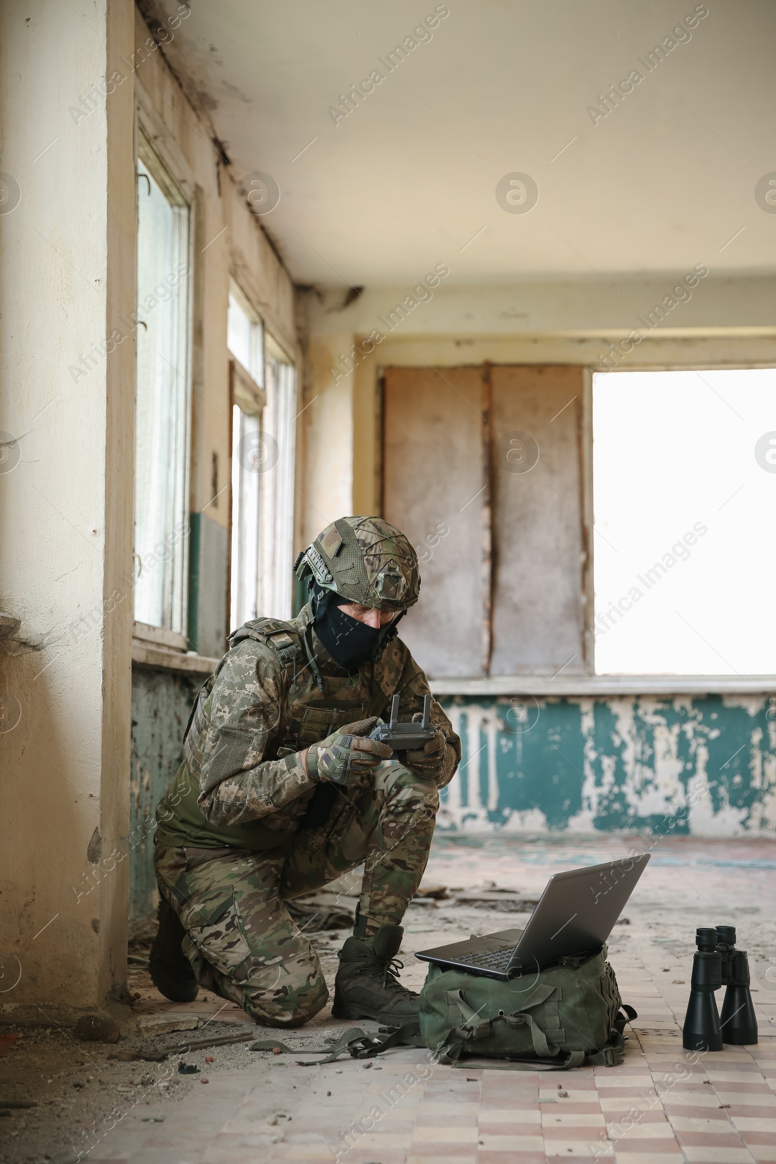 Photo of Military mission. Soldier in uniform using laptop and binoculars inside abandoned building