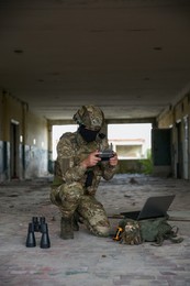 Military mission. Soldier in uniform with drone controller, laptop and binoculars inside abandoned building