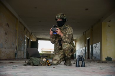 Photo of Military mission. Soldier in uniform with drone controller, laptop and binoculars inside abandoned building