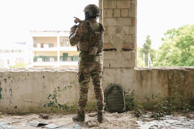 Photo of Military mission. Soldier in uniform with binoculars inside abandoned building, back view