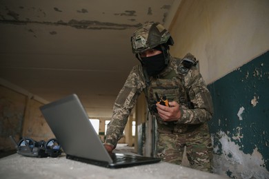 Military mission. Soldier in uniform with radio transmitter using laptop at table inside abandoned building