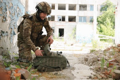 Military mission. Soldier in uniform near abandoned building outdoors, space for text
