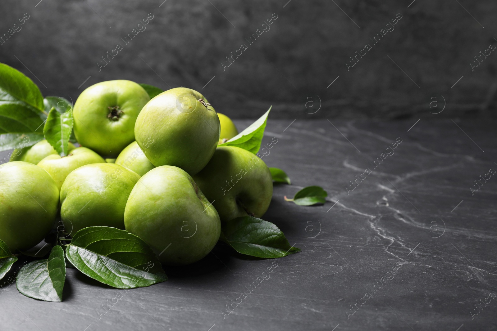 Photo of Ripe green apples with leaves on dark grey table. Space for text