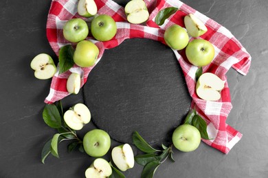 Photo of Ripe green apples, leaves and towel on black textured table, flat lay. Space for text