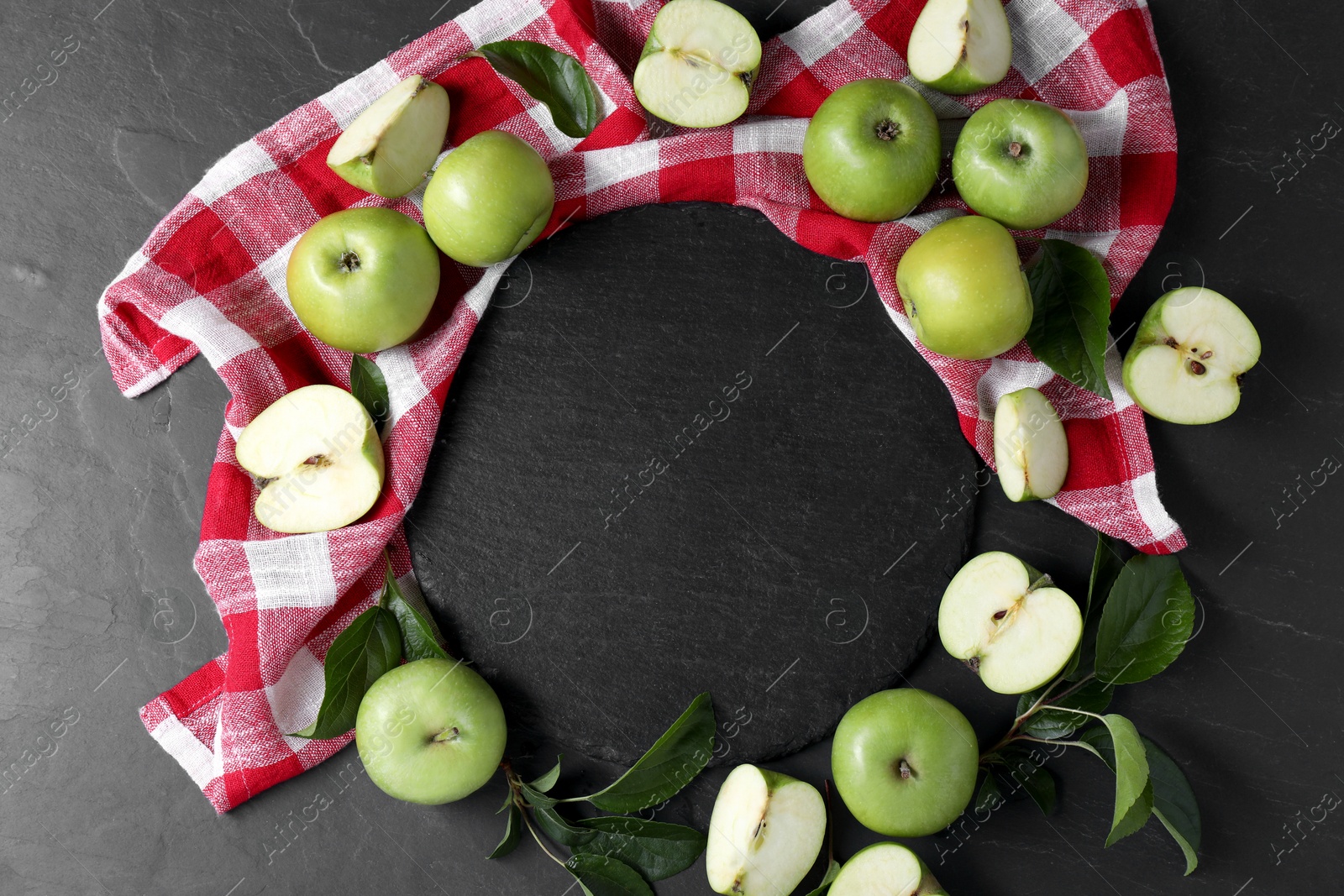 Photo of Ripe green apples, leaves and towel on black textured table, flat lay. Space for text