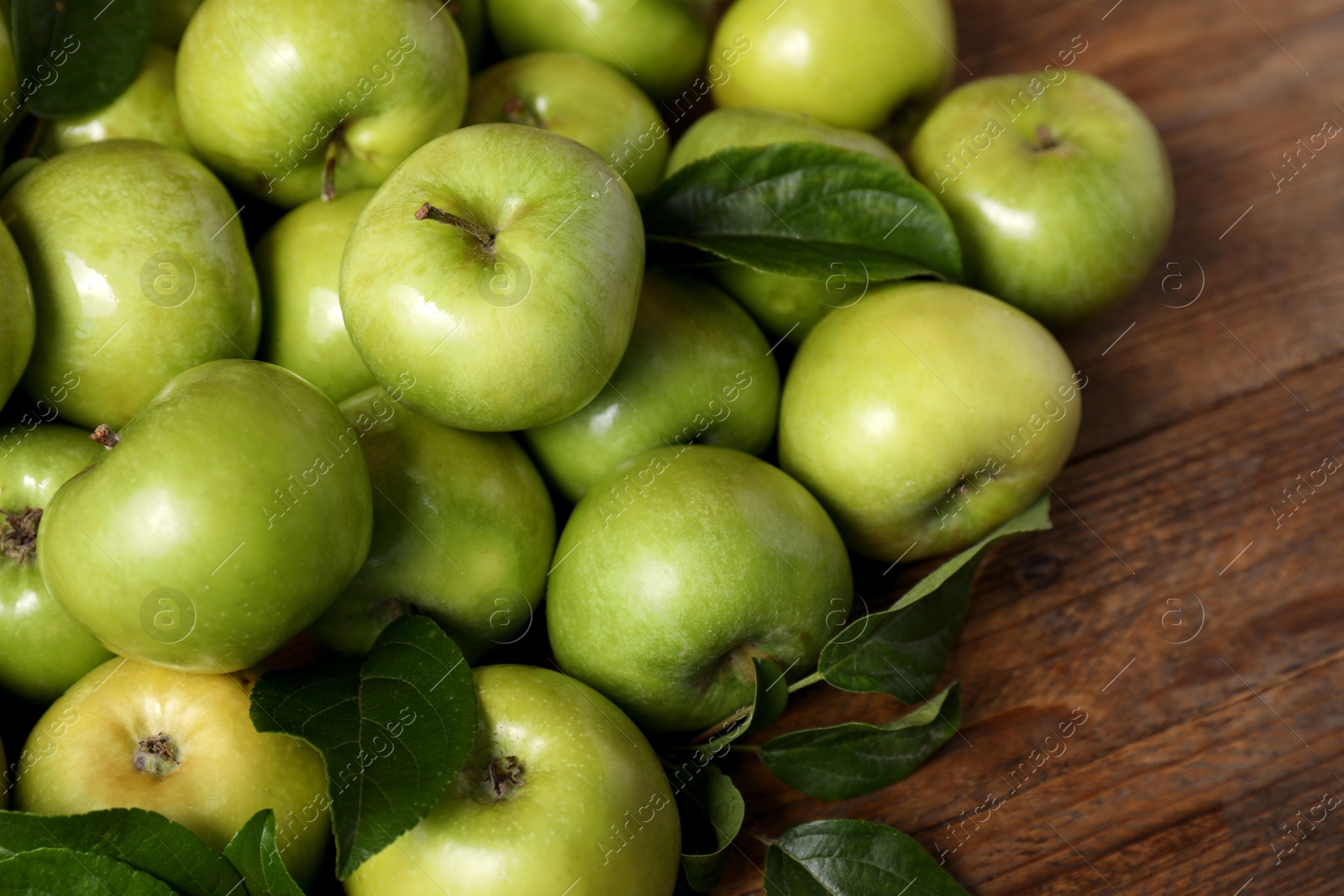 Photo of Ripe green apples with leaves on wooden table, closeup