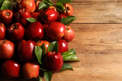 Photo of Fresh ripe red apples with leaves on wooden table. Space for text