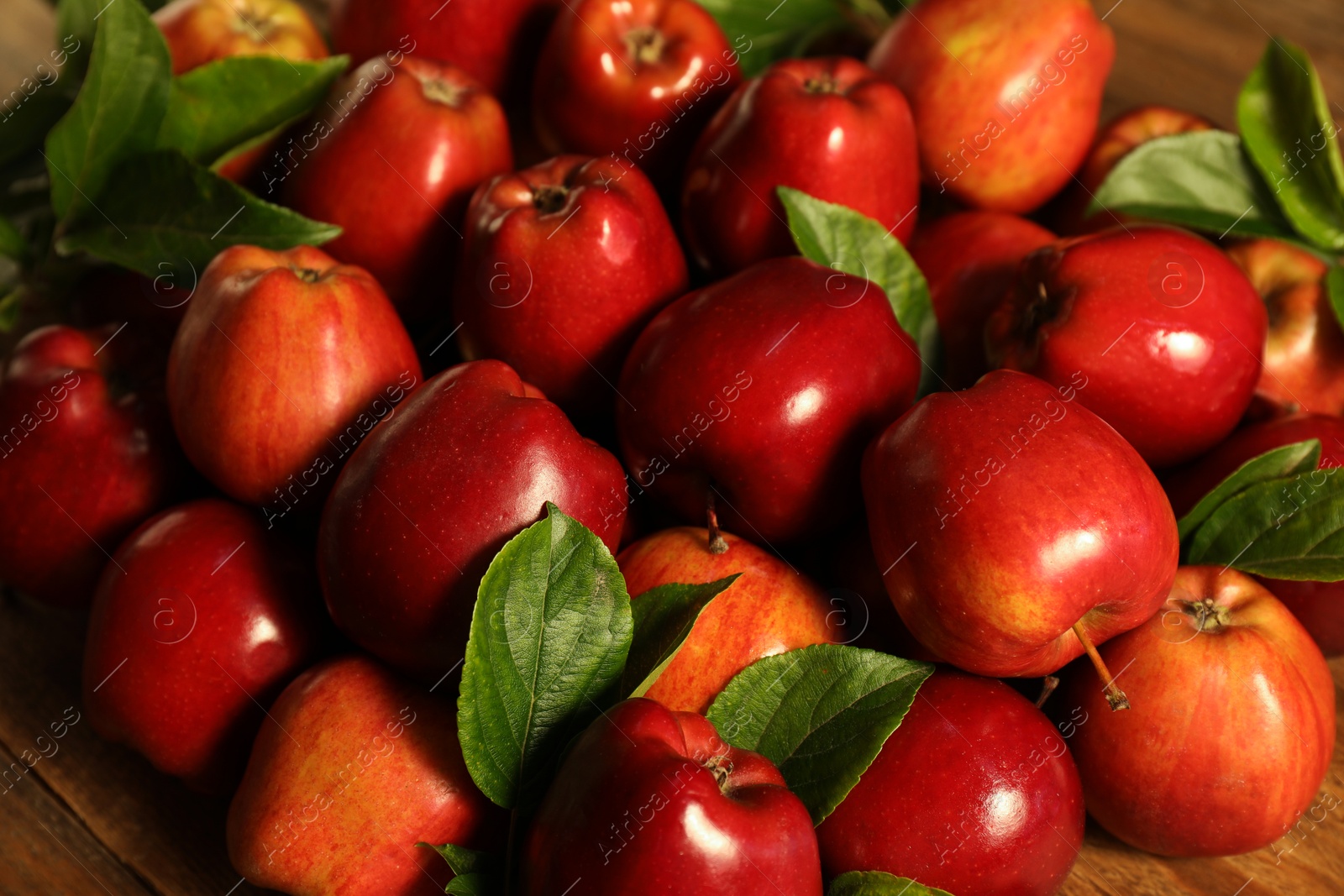 Photo of Fresh ripe red apples with leaves on wooden table, closeup