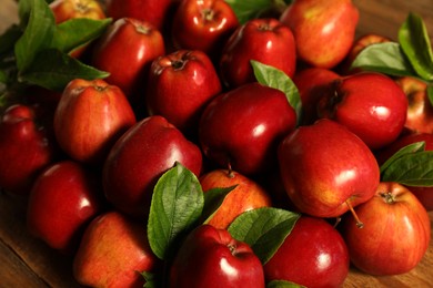 Fresh ripe red apples with leaves on wooden table, closeup