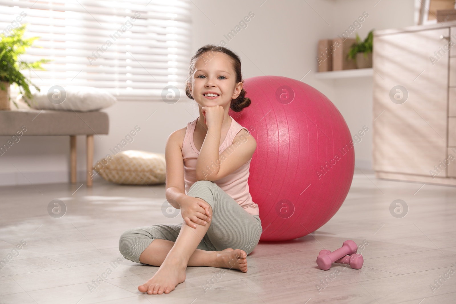 Photo of Cute little girl near dumbbells and fit ball at home