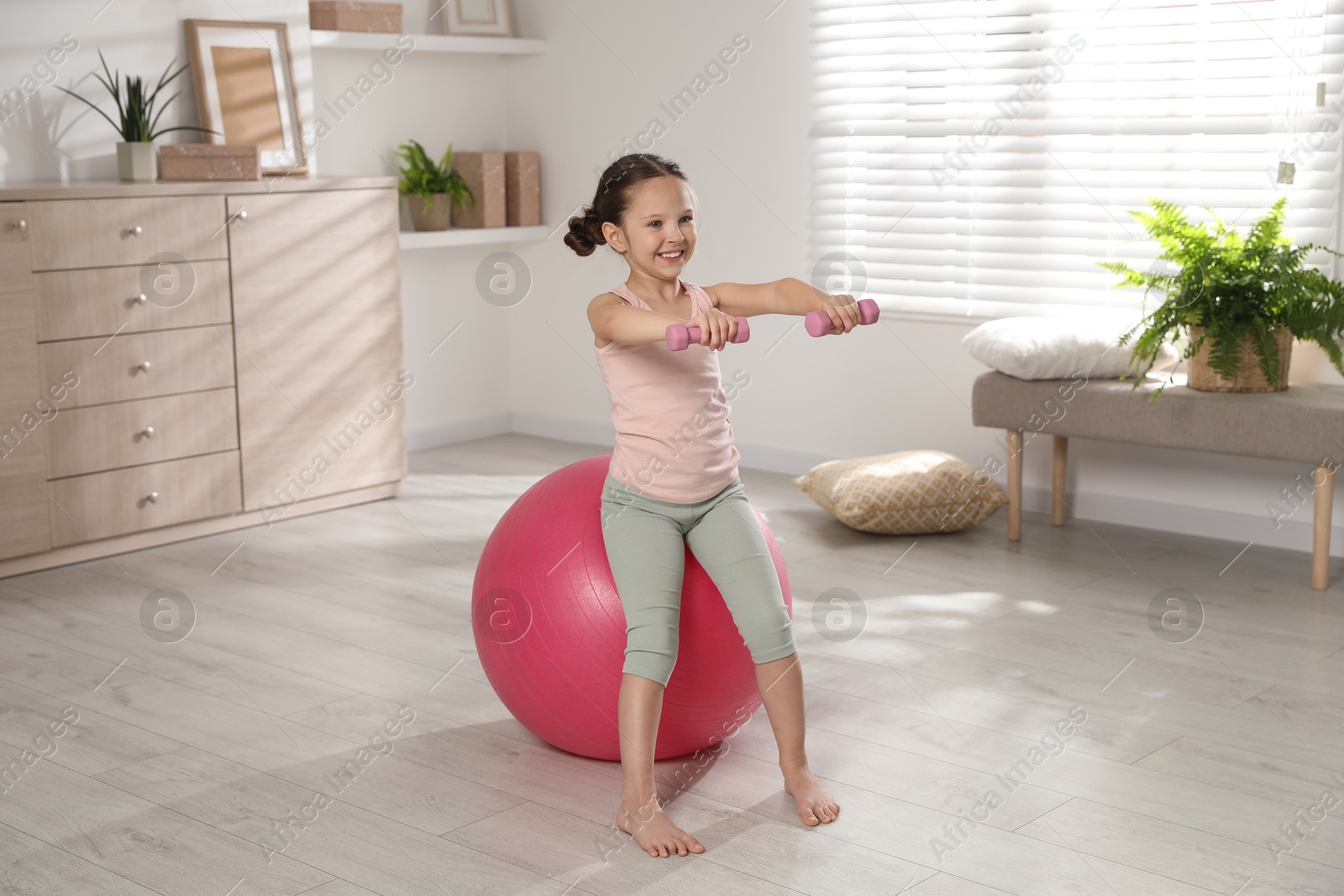 Photo of Cute little girl doing exercises with dumbbells and fit ball at home