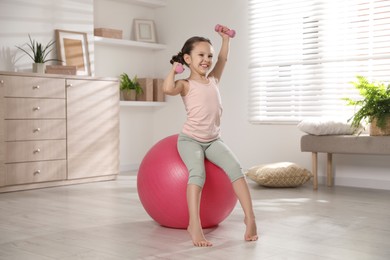 Cute little girl doing exercises with dumbbells and fit ball at home