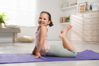 Photo of Cute little girl stretching herself on mat at home