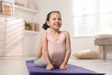 Photo of Cute little girl stretching herself on mat at home