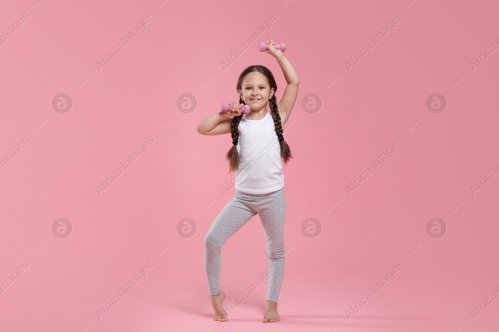 Photo of Cute little girl with dumbbells on pink background